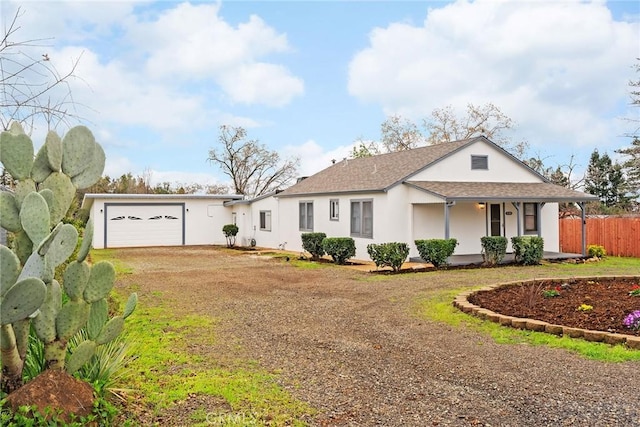 view of front facade featuring stucco siding, a porch, fence, a garage, and driveway