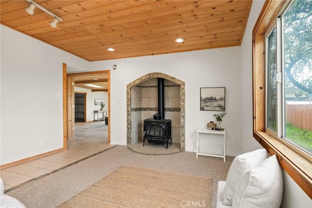 unfurnished living room with a wood stove, carpet, rail lighting, and wood ceiling