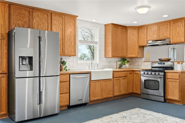 kitchen with under cabinet range hood, appliances with stainless steel finishes, light countertops, and a sink