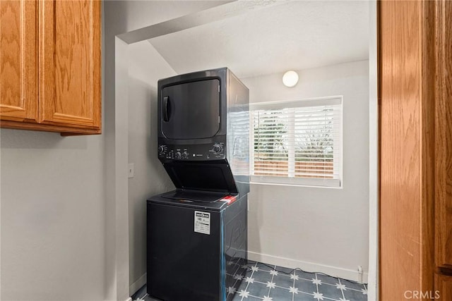 clothes washing area featuring cabinet space, baseboards, stacked washer and dryer, and tile patterned floors