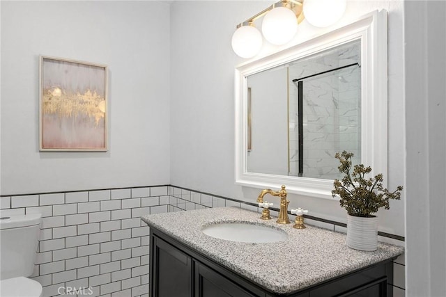 full bathroom featuring toilet, a wainscoted wall, walk in shower, vanity, and tile walls