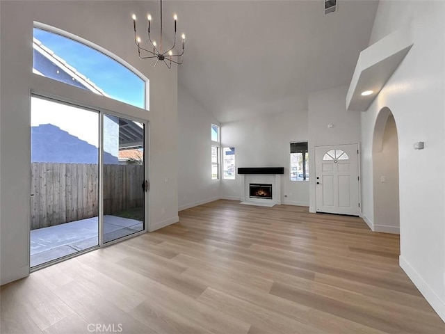 unfurnished living room with a warm lit fireplace, light wood finished floors, visible vents, and a towering ceiling