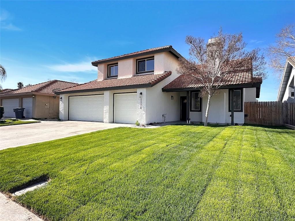 view of front of home featuring driveway, a tile roof, fence, a front yard, and stucco siding