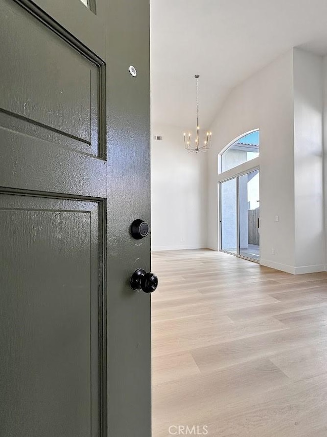 interior space featuring visible vents, baseboards, wood finished floors, an inviting chandelier, and vaulted ceiling