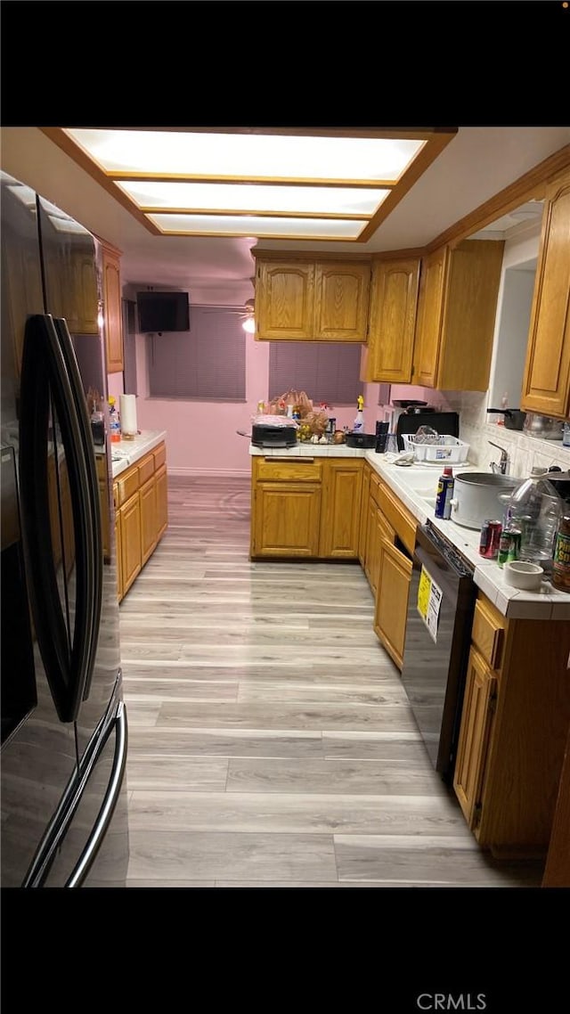 kitchen featuring light wood-style floors, brown cabinetry, light countertops, and black appliances