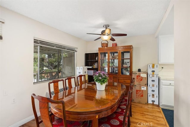 dining area featuring a textured ceiling, light wood-style floors, baseboards, and ceiling fan