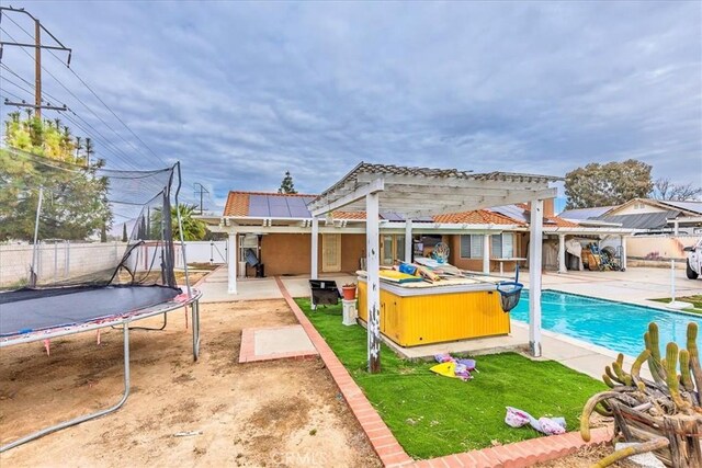 rear view of house featuring a hot tub, a fenced backyard, a trampoline, a patio area, and a pergola