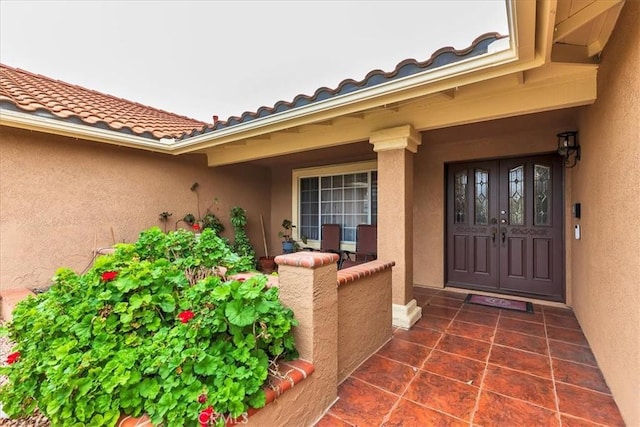 doorway to property with a tile roof, a porch, and stucco siding