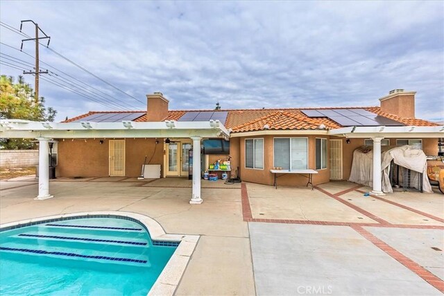 back of property featuring french doors, a patio area, solar panels, and stucco siding