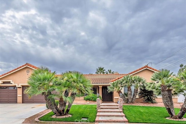 view of front facade with concrete driveway, a front yard, a tile roof, and stucco siding