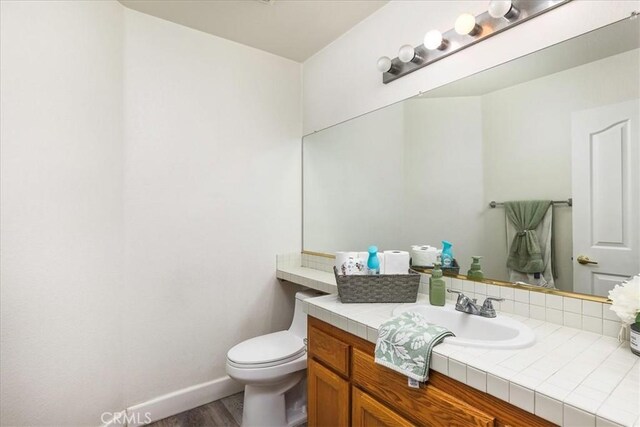 bathroom with toilet, baseboards, wood finished floors, and vanity