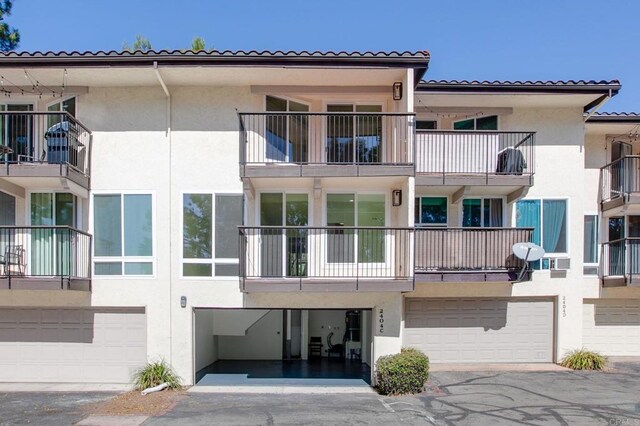 exterior space featuring an attached garage, driveway, a tile roof, and stucco siding