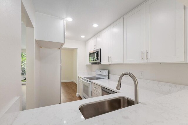 kitchen featuring light stone counters, white range with electric cooktop, stainless steel microwave, light wood-style floors, and a sink