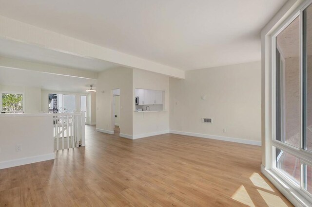 spare room featuring beam ceiling, visible vents, light wood-style flooring, and baseboards