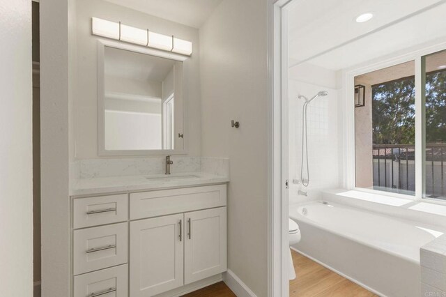 full bath featuring bathing tub / shower combination, toilet, vanity, wood finished floors, and baseboards