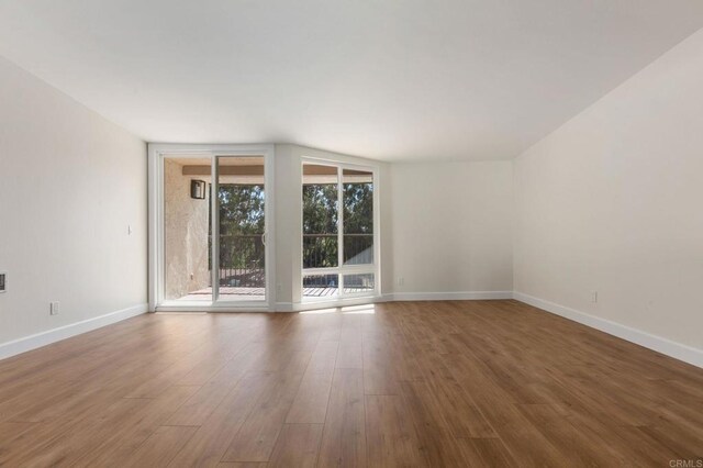 unfurnished room with expansive windows, wood finished floors, and baseboards