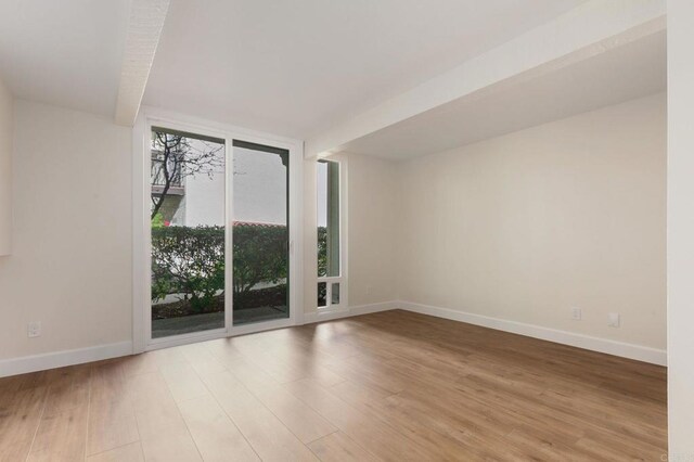 unfurnished room with expansive windows, light wood-style flooring, and baseboards