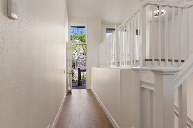 hallway with a textured wall, wood finished floors, and baseboards