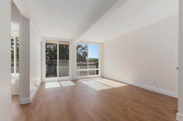 empty room with baseboards, floor to ceiling windows, beamed ceiling, and wood finished floors