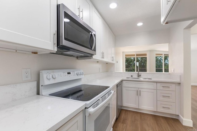 kitchen featuring a sink, appliances with stainless steel finishes, light wood finished floors, and white cabinetry