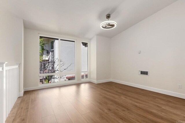 unfurnished room with baseboards, visible vents, light wood-style flooring, and vaulted ceiling