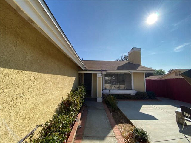 property entrance with a patio area, fence, a chimney, and stucco siding