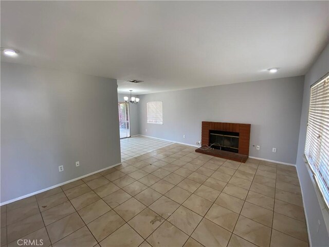 unfurnished living room with a brick fireplace, baseboards, visible vents, and a chandelier