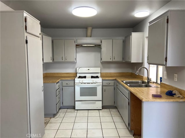 kitchen with light tile patterned floors, white gas range, light countertops, gray cabinetry, and a sink