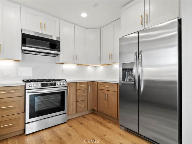 kitchen with appliances with stainless steel finishes, white cabinetry, light countertops, and light wood-style floors