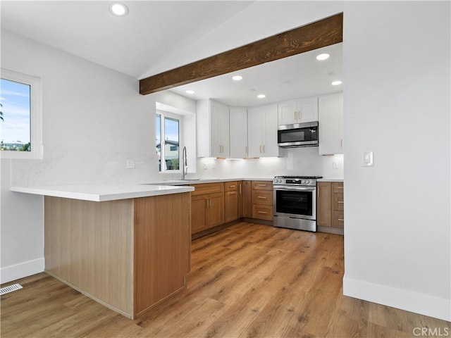 kitchen featuring decorative backsplash, appliances with stainless steel finishes, a peninsula, and white cabinetry