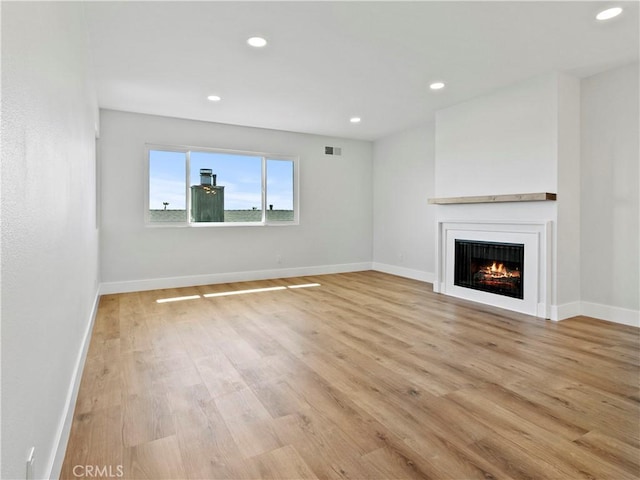 unfurnished living room featuring visible vents, baseboards, recessed lighting, a warm lit fireplace, and light wood-style floors