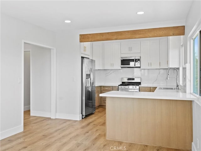 kitchen featuring light wood-style flooring, a peninsula, stainless steel appliances, and a sink