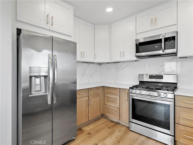 kitchen featuring decorative backsplash, light countertops, light wood-style floors, appliances with stainless steel finishes, and white cabinetry