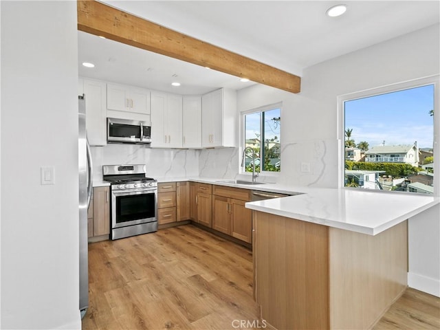 kitchen with beamed ceiling, a sink, stainless steel appliances, a peninsula, and light wood finished floors