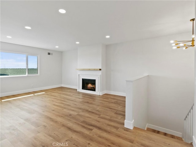 unfurnished living room with visible vents, recessed lighting, light wood-type flooring, and a warm lit fireplace