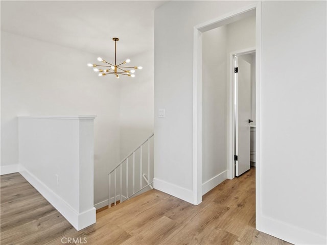 hall featuring an upstairs landing, a chandelier, baseboards, and wood finished floors