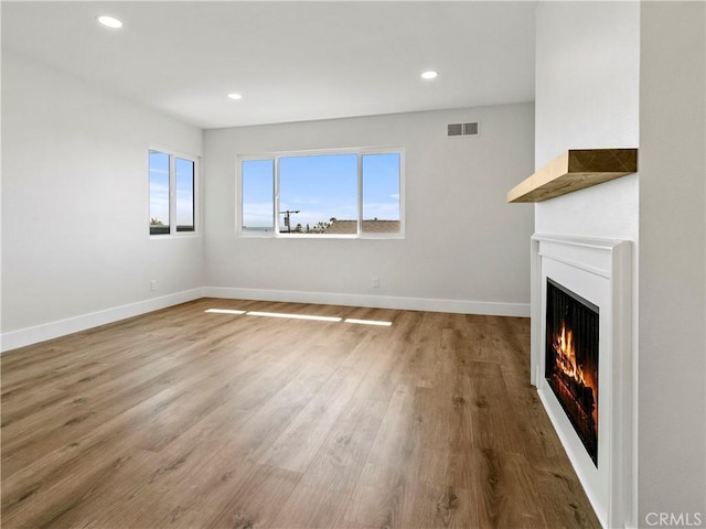 unfurnished living room with plenty of natural light, baseboards, visible vents, and a lit fireplace