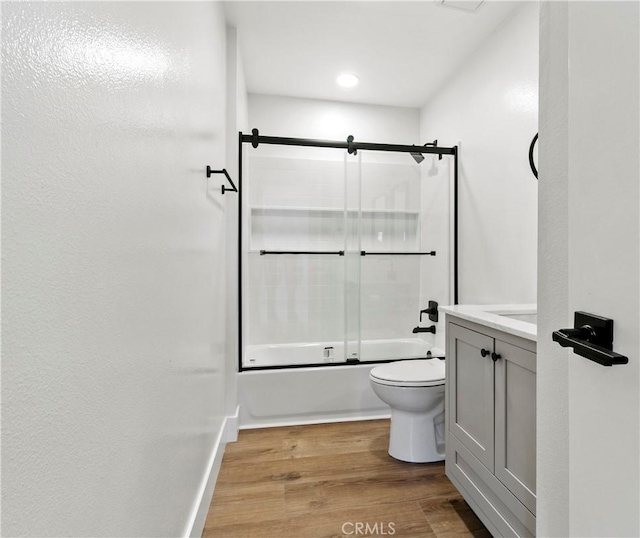 full bathroom featuring toilet, wood finished floors, combined bath / shower with glass door, baseboards, and vanity