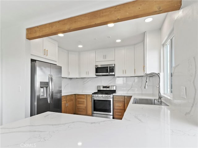 kitchen featuring beamed ceiling, a sink, appliances with stainless steel finishes, decorative backsplash, and light stone countertops