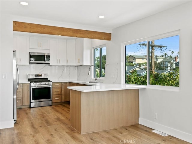 kitchen with a sink, light wood-style floors, appliances with stainless steel finishes, and a peninsula