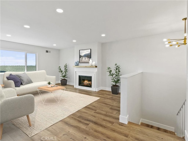 living area featuring wood finished floors, baseboards, visible vents, recessed lighting, and a lit fireplace