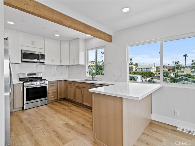 kitchen with light wood-type flooring, beamed ceiling, a sink, stainless steel appliances, and a peninsula