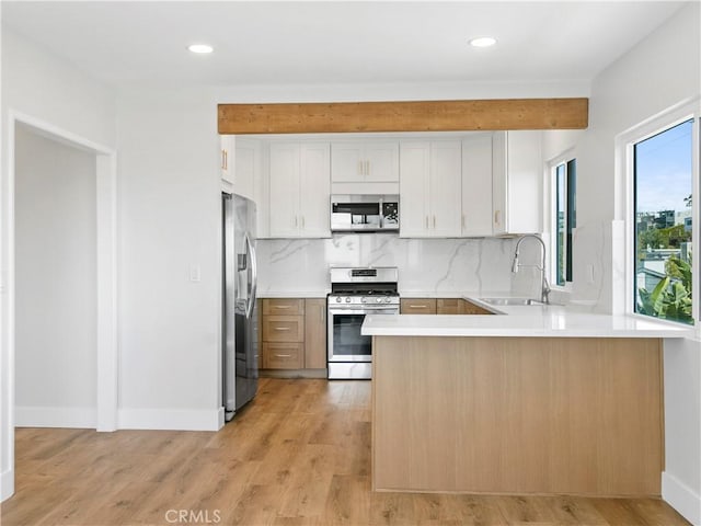 kitchen with a sink, tasteful backsplash, light wood-style floors, appliances with stainless steel finishes, and a peninsula