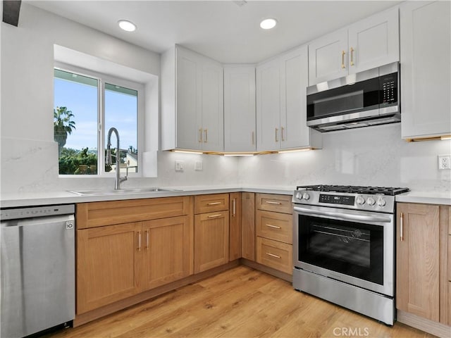 kitchen featuring light wood finished floors, a sink, stainless steel appliances, light countertops, and backsplash