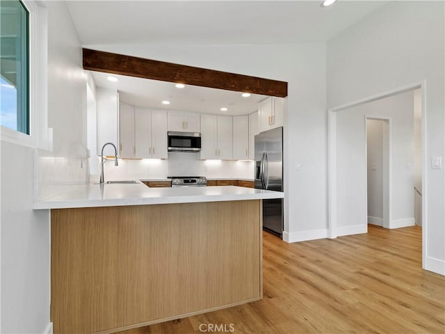 kitchen featuring light wood finished floors, light countertops, a peninsula, stainless steel appliances, and a sink