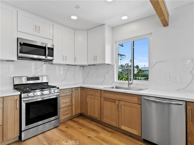 kitchen featuring light wood-style flooring, a sink, stainless steel appliances, light countertops, and white cabinets