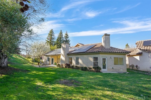 rear view of property with roof mounted solar panels, a patio, a tiled roof, and a lawn