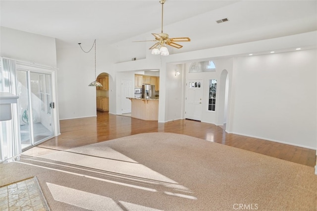 living area with visible vents, arched walkways, a ceiling fan, light wood-style flooring, and high vaulted ceiling