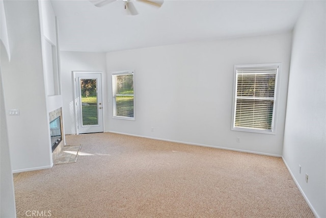 unfurnished room with carpet floors, baseboards, ceiling fan, and a tiled fireplace