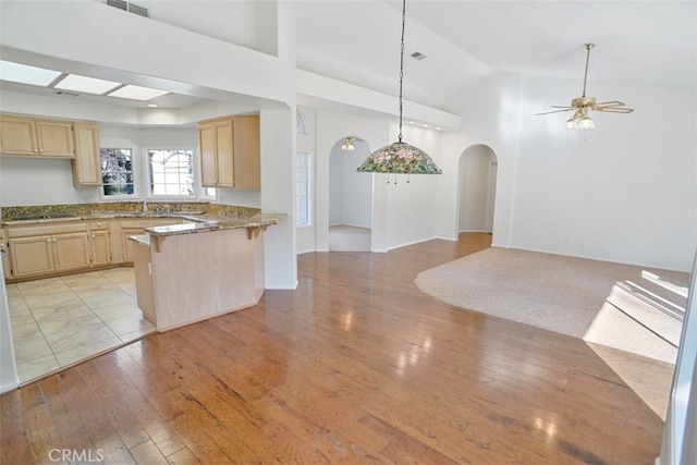 kitchen with arched walkways, light wood-style flooring, light brown cabinetry, open floor plan, and a peninsula